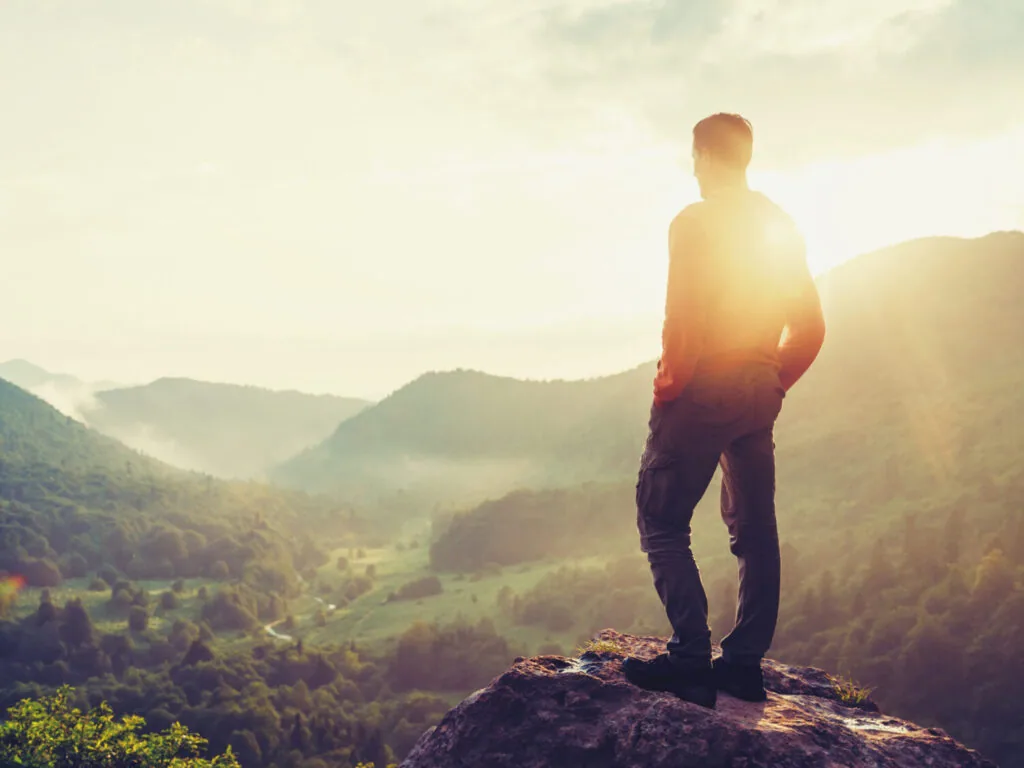 Traveler young man standing in the summer mountains at sunset and enjoying view of nature. Image with instagram color